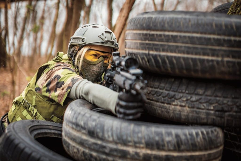joueur-airsoft-sur-le-terrain-avec-une-replique-airsoft-cache-derriere-des-pneus-pour-des-tirs-discrets
